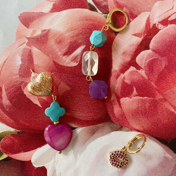 halflange gouden oorbellen met roze en turkooise edelstenen kralen. Liggend op een blad van bloemen