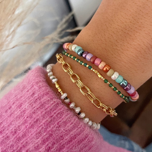 een pols met kleurrijke armbandjes van parels en roze blauwe paarse en lichtgroene kralen
