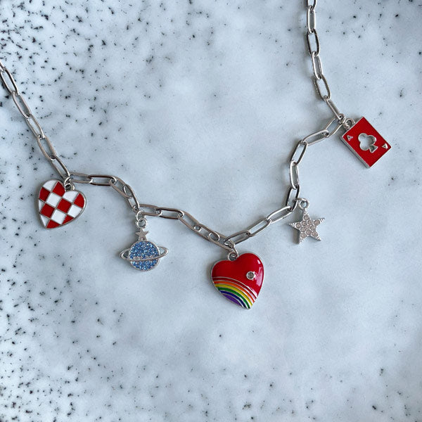 Een zilveren bedelketting met gekleurde bedels waaronder een rood wit hart, een planeet en een sterretje en een regenboog hart. 