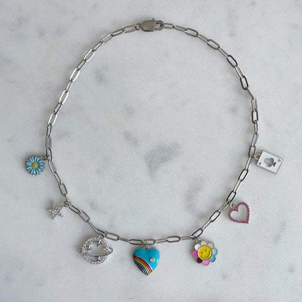 Een zilveren bedelketting met gekleurde bedels waaronder een regenboog hart, bloem, een ster en een planeet met zirconia steentjes. 