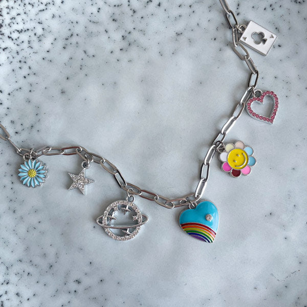 Een zilveren bedelketting met gekleurde bedels waaronder een regenboog hart, bloem, een ster en een planeet met zirconia steentjes. 