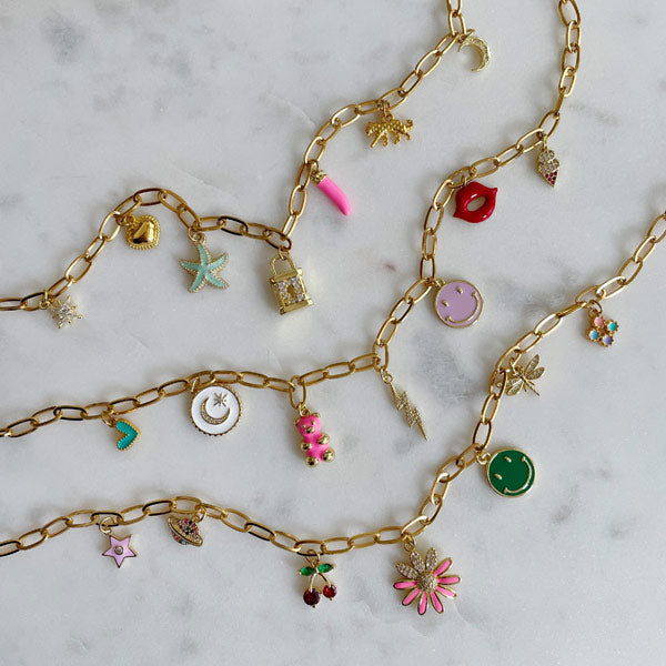 Gouden schakelketting met gekleurde bedels waaronder een zeester, roze tandje, hartje, panter en maantje. 