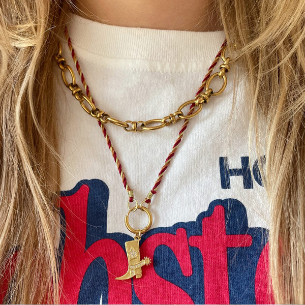 Ketting gemaakt van geweven twisted koord en een gouden ringsluiting. Afgewerkt met fijn metallic koord. Aan de sluiting hangt een gouden westernlaarsje.