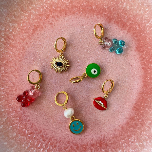 gouden oorbellen met een rode mond, een gummybear in het blauw en rood op een roze bord