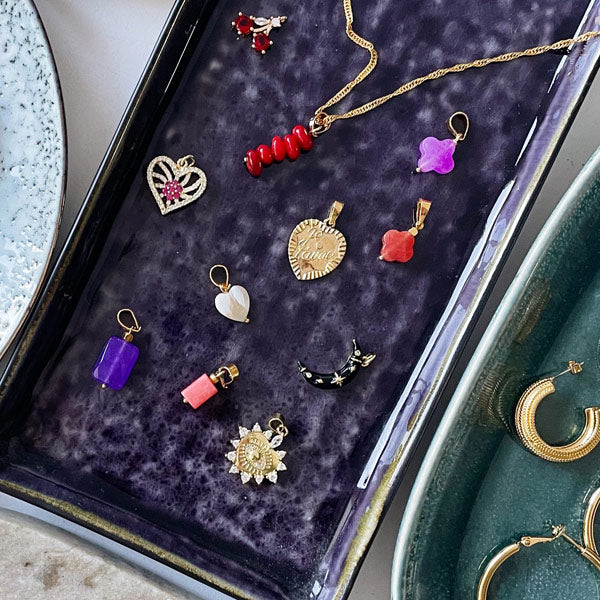 een gouden bedel van een hart op een paars bord met verschillende ketting hangers van roze agaat en blauwe jade
